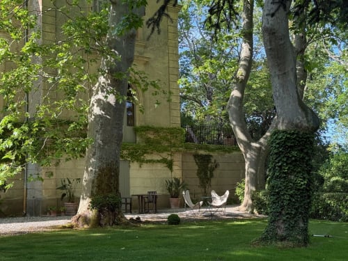 Cour ombragée du Domaine de Montlaur avec grands arbres, salon de détente et bâtisse en pierre couverte de lierre à Val-de-Dagne