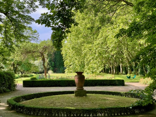 Jardin formel du Domaine de Montlaur avec urne en terre cuite, haies taillées, allées bordées d'arbres et coin salon