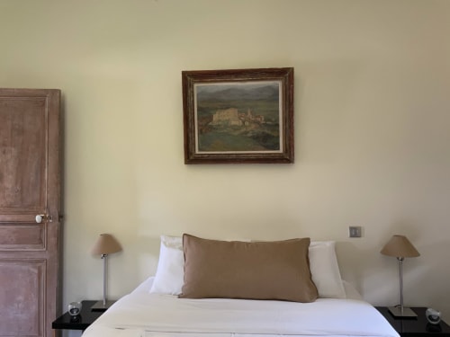 Chambre au Domaine de Montlaur avec lit blanc, oreiller marron, tables de nuit et lampes, décorée d'une gravure de château
