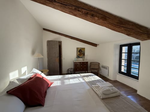 Chambre spacieuse de la villa Domaine de Montlaur avec poutres apparentes, lit aux oreillers rouges, mobilier en bois et encadrement noir