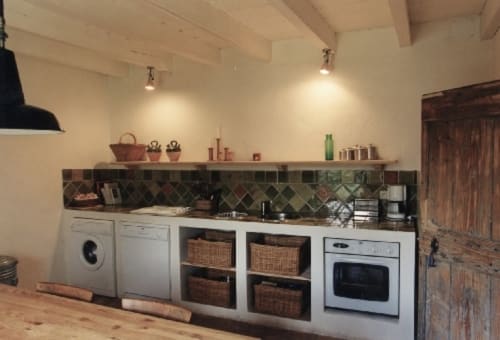 Cuisine moderne aux armoires blanches, paniers tressés, appareils inox et carrelage géométrique foncé à Domaine de