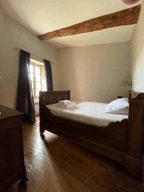 Chambre de la villa La Maison du Village au Domaine de Montlaur avec lit en bois, poutres apparentes, linge blanc et fenêtre.