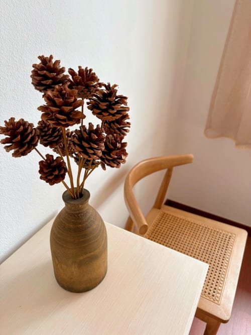 Arranjo de pinhas secas em vaso de madeira sobre mesa branca na Quinta Vale da Paz, Azambuja
