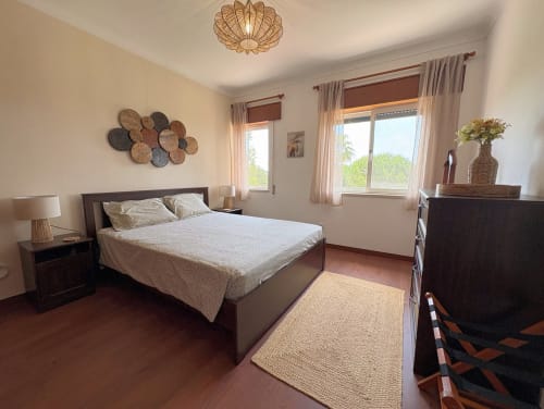 Quarto claro na Quinta Vale da Paz BnB em Azambuja com cama queen, móveis de madeira escura, arte têxtil na parede e tons de terracota