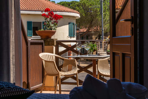 Sunny terrace at Albergo Al Cinghiale with wooden dining table, striped chairs, red flowers, and white-walled hotel building