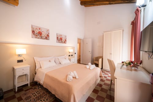 Bright bedroom at Albergo Al Cinghiale with peach bedding, white furniture, exposed wooden beams, and modern amenities in