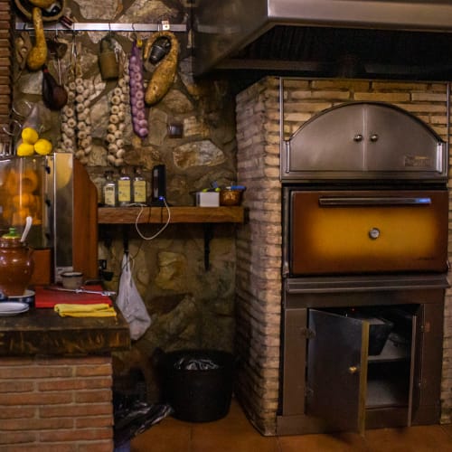 Cocina rústica del Hotel Balcón De Los Montés en Colmenar con embutidos colgantes, paredes de ladrillo y horno antiguo