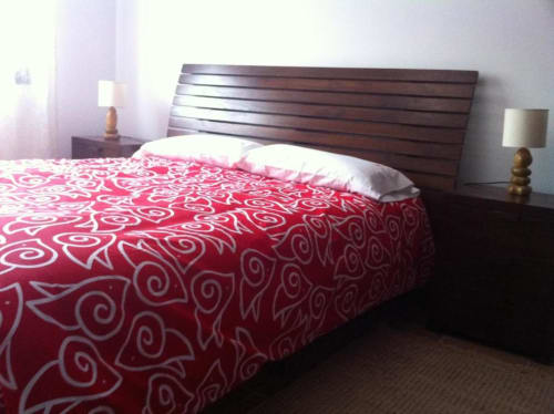 Dormitorio moderno con cama de madera oscura, ropa de cama roja con estampado y almohadas blancas en el apartamento rural Alojamientos Botica