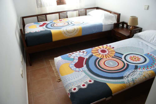 Dormitorio en Alojamientos Botica Rural con dos camas de madera, ropa de cama con patrones coloridos, suelo de azulejos y estilo rústico