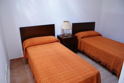 Habitación doble con colchas naranjas, cabeceros de madera oscura y lámpara de noche en Alojamientos Botica Rural, La Cabrera