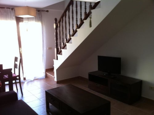 Luminosa sala de estar del apartamento La Cabrera con escalera de madera, muebles oscuros y piso de azulejos
