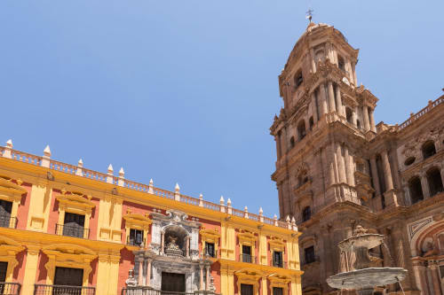 Arquitectura colonial colorida en Colmenar con un edificio amarillo-rojo vibrante y una ornada torre de catedral de piedra bajo el cielo azul