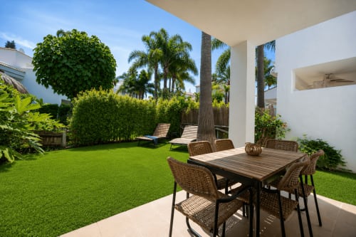 Patio de jardín estilo Maui en BH Marbella con mesa de comedor, tumbonas, palmeras y césped exuberante