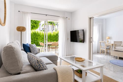 Luminosa sala de estar moderna en Maui by BH Marbella con sofá beige, TV de pantalla plana y vistas al océano desde la terraza