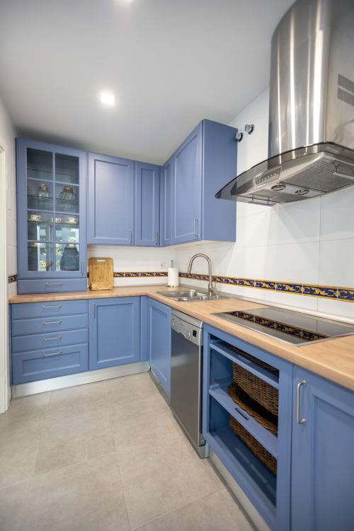 Moderna cocina azul con encimeras de madera, electrodomésticos de acero inoxidable y azulejos decorativos en la villa de Maui, BH