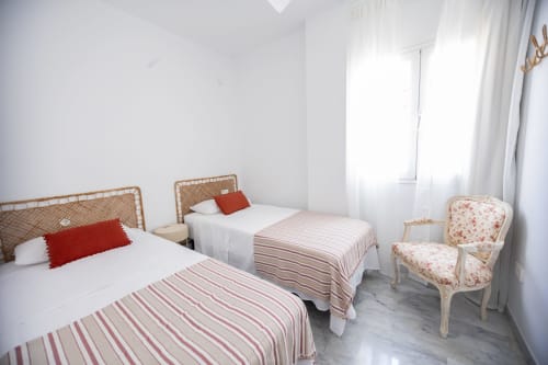 Luminoso dormitorio doble en Maui by BH Marbella con cabeceros de ratán, ropa de cama a rayas y cortinas con vistas al mar