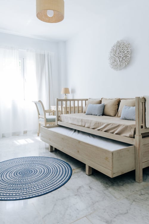 Luminoso dormitorio en BH Marbella con cama balinesa de madera, alfombra circular azul y vistas al mar