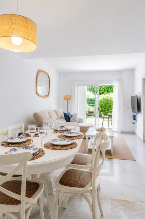 Comedor luminoso en cabaña de Maui en BH Marbella con mesa redonda blanca, manteles tejidos y vista al mar a través de puertas de cristal