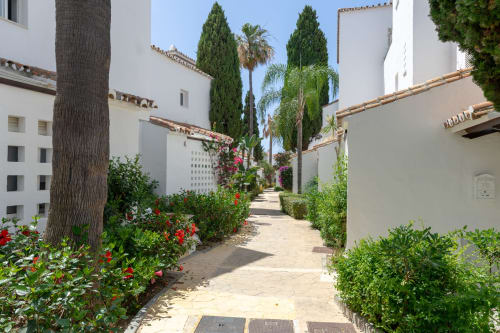Sendero exuberante del complejo BH Marbella en Marbella con villas blancas, plantas tropicales y flores coloridas