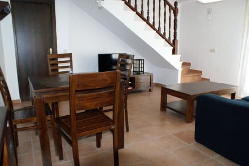 Mesa y sillas de madera rústica en salón diáfano con escaleras en Alojamientos Botica Rural, La Cabrera