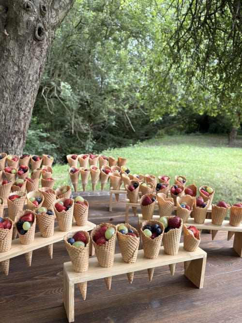 Cornets de gaufre garnis de fruits disposés sur des tables en bois dans l'espace de réception du jardin du Domaine du Tertre Ychot, Dol de Bretagne