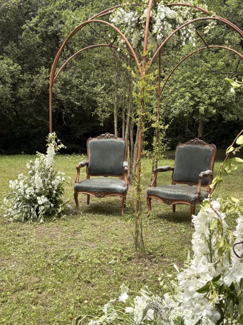 Zone de réception du jardin au Domaine du Tertre Ychot avec pergola métallique ornée, chaises élégantes et plantes à fleurs blanches à Dol