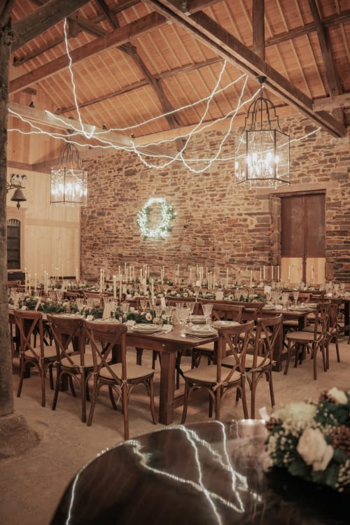Élégante salle de réception en pierre au Domaine du Tertre Ychot avec tables longues décorées, luminaires suspendus et couronne de verdure