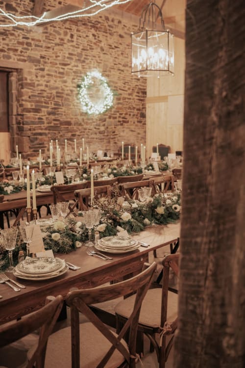 Salle de réception élégante au Domaine du Tertre Ychot avec murs en brique, tables illuminées à la bougie, fleurs blanches et couronne festive