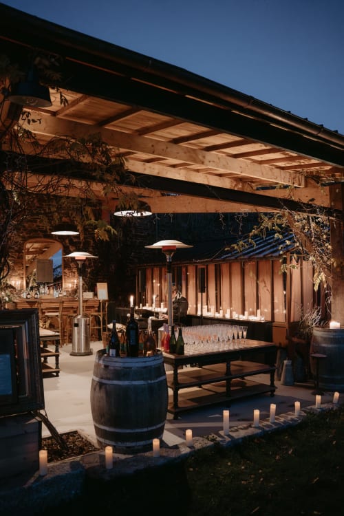 Salle de réception en soirée au Domaine du Tertre Ychot avec table en tonneau, service de vin et chandelles sous poutre bois