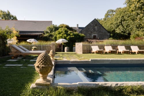 Piscine du Domaine du Tertre Ychot avec chapeau de pierre, bains de soleil, parasols et bâtiments historiques bretons à Dol de Bretagne
