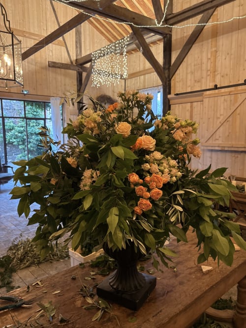 Élégant arrangement floral avec roses oranges et feuillage dans une urne noire à la salle de réception du Domaine du Tertre Ychot, Dol de