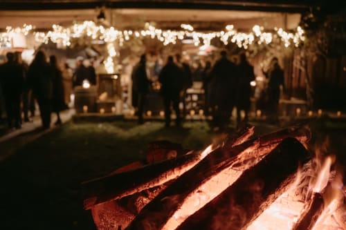 Ambiance chaleureuse autour du feu de camp à la salle de réception du Domaine du Tertre Ychot à Dol de Bretagne, illuminée de guirlandes lumineuses avec les invités rassemblés