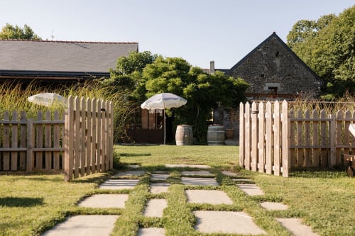 Allée de jardin avec portails en bois blanc au Domaine du Tertre Ychot à Dol de Bretagne, bâtiments en pierre et paysage soigné