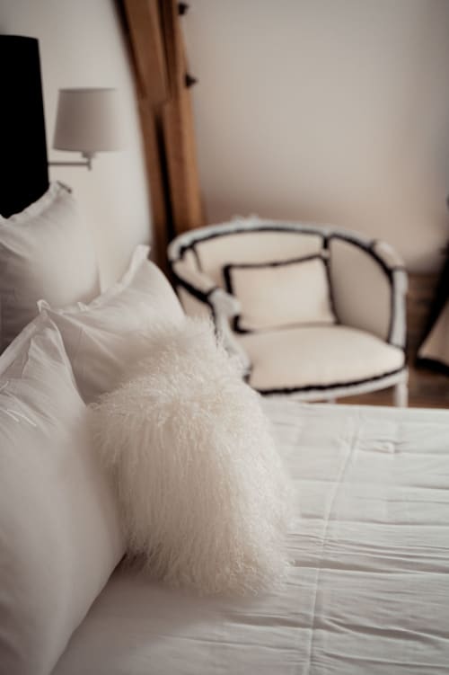 Moelleux oreillers blancs sur le lit de la chambre Les Hirondelles du Domaine du Tertre Ychot, Dol de Bretagne, avec fauteuil et lampe