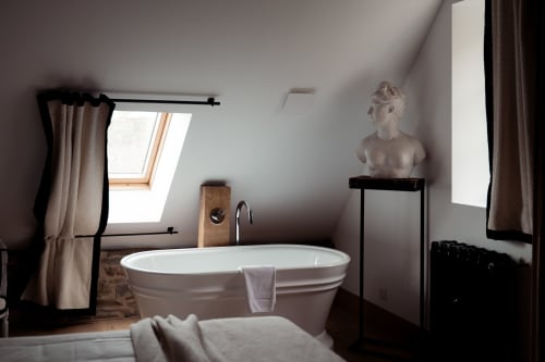 Salle de bain luxueuse sous les toits du Domaine du Tertre Ychot avec baignoire îlot, puits de lumière et décoration classique à Dol de Bretagne.