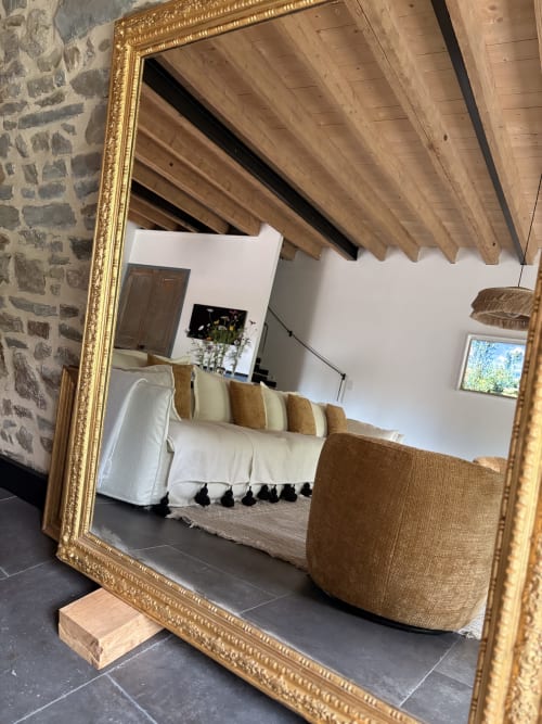 Miroir aux cadre doré reflétant une chambre cosy de Domaine du Tertre Ychot avec poutres apparentes, canapé blanc et murs en pierre à Dol