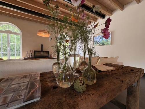 Salle élégante avec fleurs fraîches en vases de verre sur table rustique, cheminée et vue sur le jardin du Domaine du Tertre Ychot