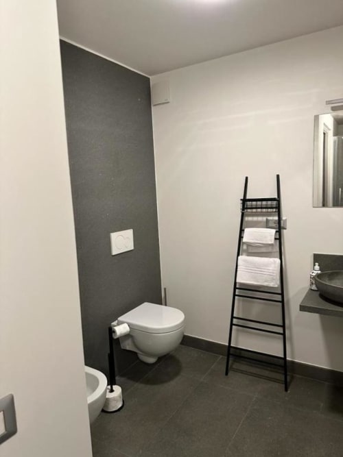 Moderno bagno con wc sospeso, parete di piastrelle scure, scaletta nera per asciugamani e lavabo nell'appartamento di una B&B a Orvieto