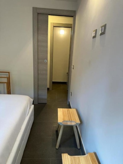 Stretto corridoio dell'appartamento a 2 camere da letto a Il Giardinetto di Elelú a Orvieto, con letto bianco, sgabello in legno e porta aperta