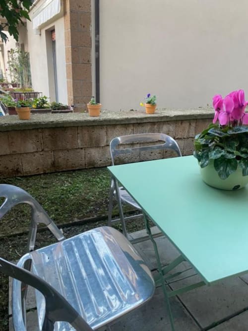 Area pranzo esterna di Il Giardinetto a Orvieto con tavoli color menta, sedie in metallo e ciclamini rosa nel giardino