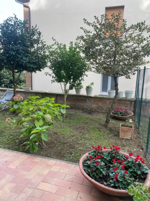 Affascinante vista del giardino di Il Giardinetto a Orvieto con fiori rossi, piante in vaso, alberi e zona lounge esterna.