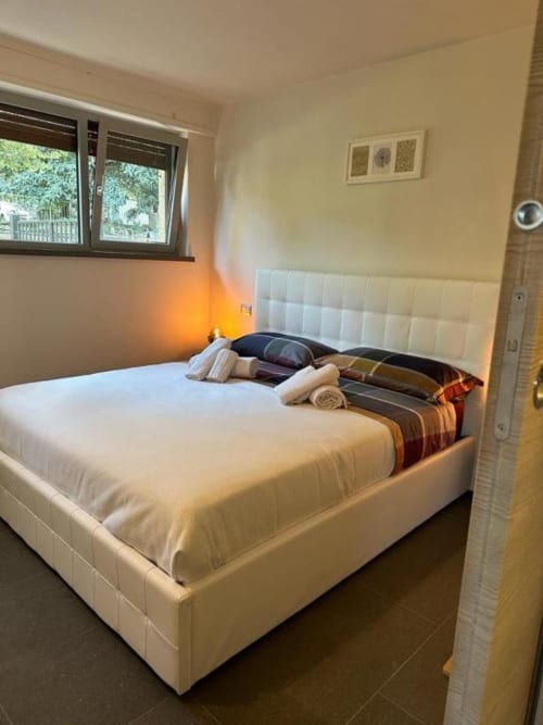 Camera luminosa con letto bianco, asciugamani arrotolati, coperta a righe e vista sul giardino a Il Giardinetto di Elelú
