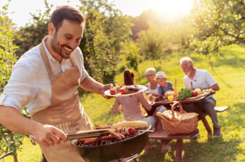 Man grilling food at Clos Céleste outdoor gathering in Normandy countryside with guests enjoying meal together