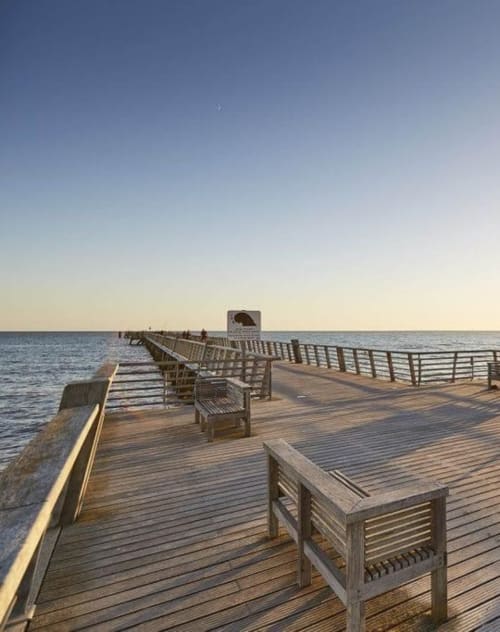 Wooden pier at Hôtel Bar La Pinède in Saint-Jean-de-Monts with benches overlooking calm sea at sunset