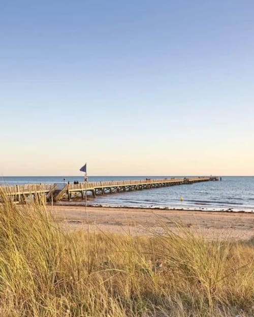 Long wooden pier extending into the sea at Saint-Jean-de-Monts beach with blue flag and beach grass in foreground
