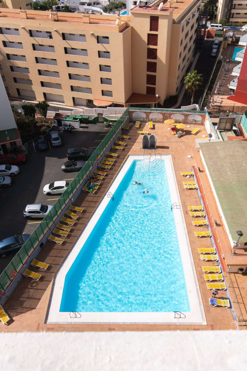 Vista aérea de piscina rectangular con tumbonas amarillas en Home Stay Gran Canaria, rodeada de terraza de barro cocido