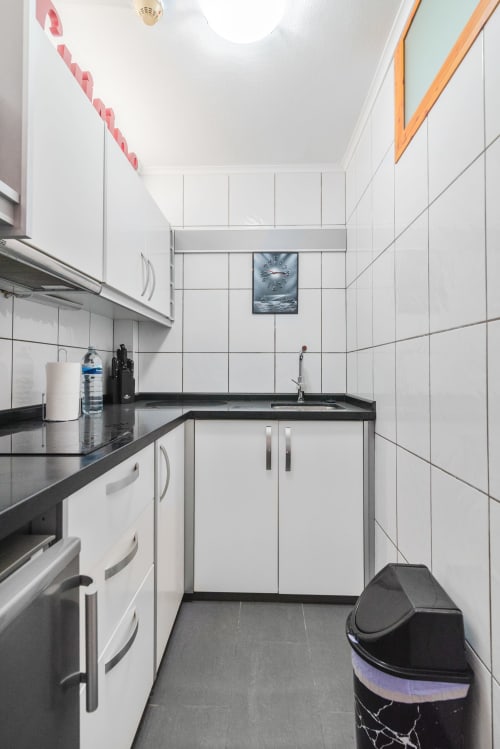 Moderna cocina blanca con encimeras negras, electrodomésticos de acero inoxidable y paredes alicatadas en San Bartolomé de Tirajana