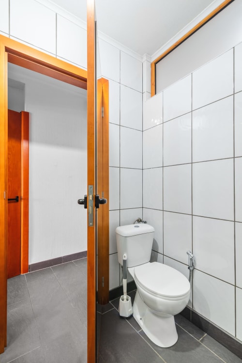 Baño moderno con paredes de azulejos blancos, inodoro blanco y marco de puerta de madera en tonos naranjas cálidos en Home Stay Gran Canaria