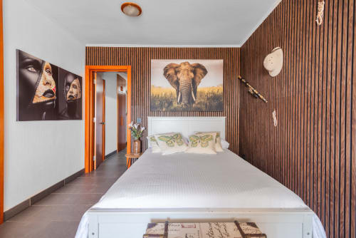 Dormitorio moderno con cama queen, pared de madera, obra de arte de elefante y puerta naranja en apartamento naturista de Gran Canaria