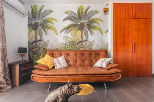 Salón moderno con sofá de cuero cognac, papel tapiz tropical con palmeras, armario naranja y estatua decorativa de perro en Home Stay